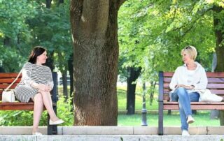 Two ladies are talking to each other while sitting on a bench in a park - How to Live a Happy Life Along with Motivation - Outstanding Way - Motivational Blogs - Motivation N You