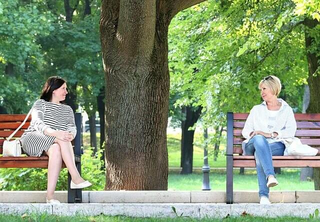 Two ladies are talking to each other while sitting on a bench in a park - How to Live a Happy Life Along with Motivation - Outstanding Way - Motivational Blogs - Motivation N You