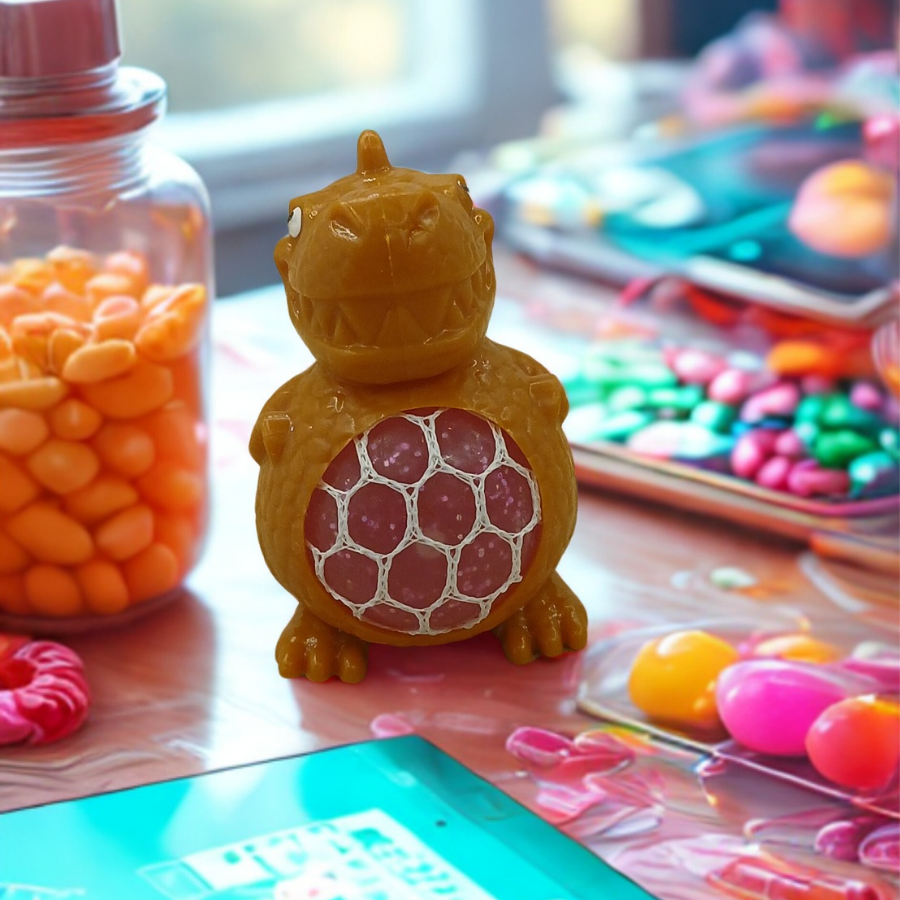 A yellow dinosaur stress toy with a pink mesh gel belly sitting on a white desk with green plants in the blurred background.