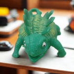 A textured green ankylosaurus dinosaur stress toy with ridges on its back sitting on an office desk setup.