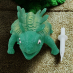 A textured green ankylosaurus dinosaur stress toy with ridges on its back sitting on an office desk setup.