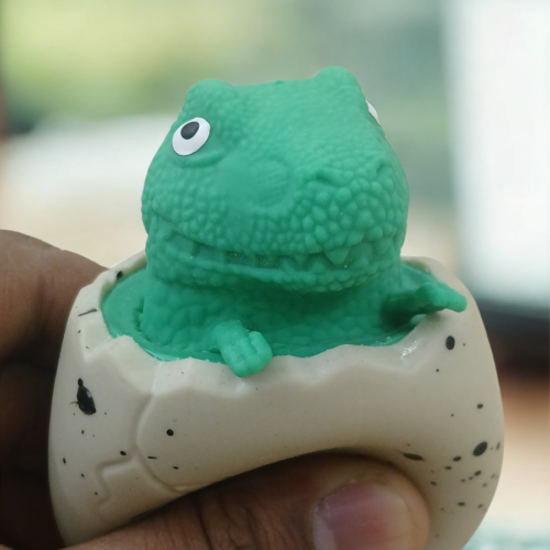 A person squeezing a speckled egg toy to reveal a green dinosaur popping out from the top.