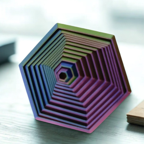 A vibrant hexagonal stress prism with tiered ridges in green, blue, and purple sitting on a professional office desk.
