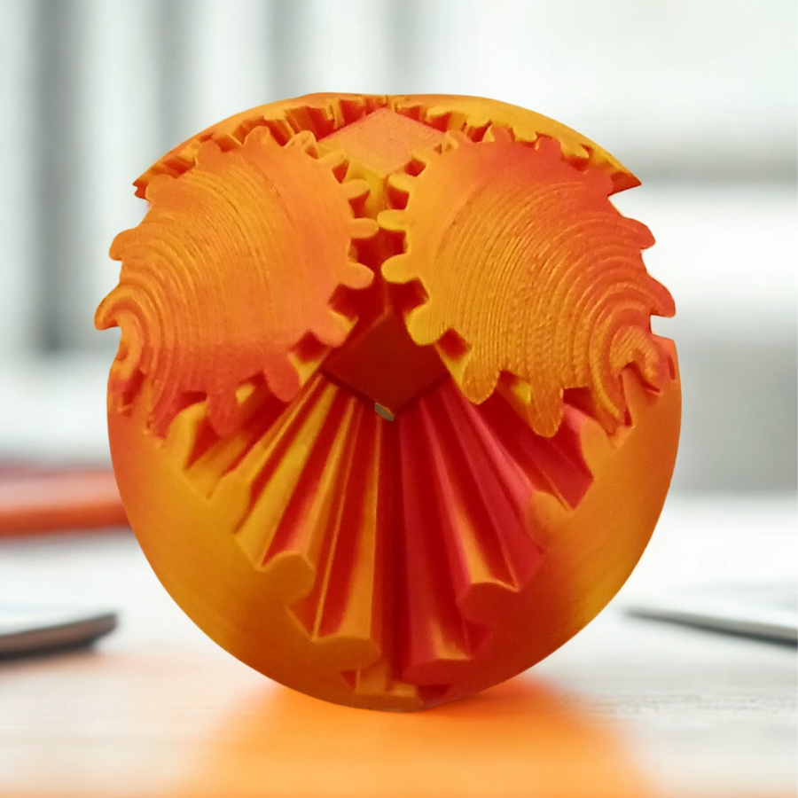 A 3D-printed spherical gear toy with orange and red gradient gears interlocking on a light wooden surface.