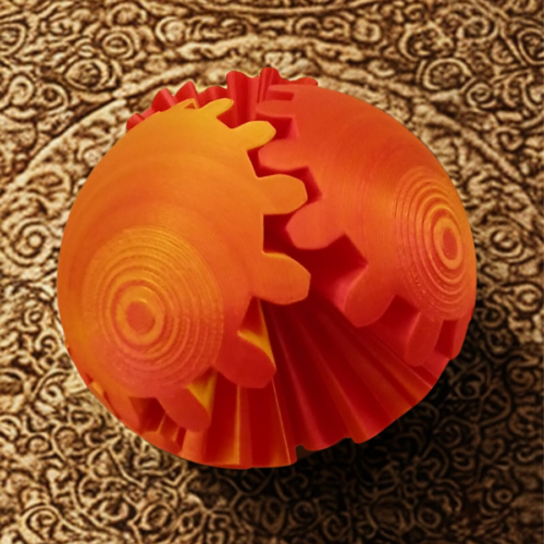 A 3D-printed spherical gear toy with orange and red gradient gears interlocking on a light wooden surface.