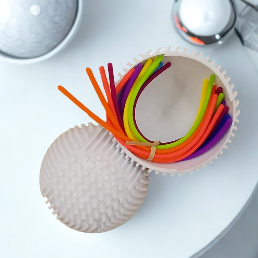 Top-down view of colorful silicone stretch strings coiled inside a light-grey textured tactile sensory sphere.